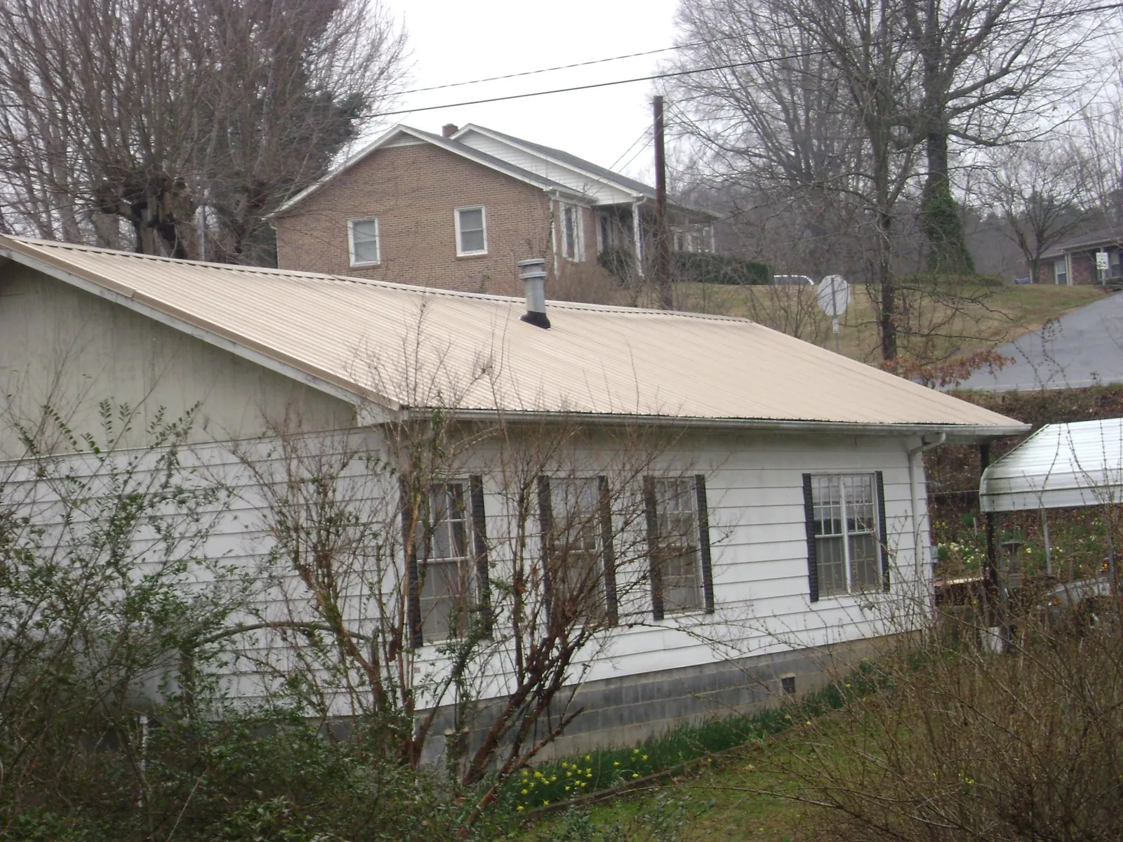 Tan metal roof on a white sided house set into a hillside — Commercial Roofing by Roofing Brothers in Junction City